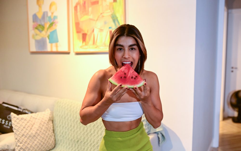 Kakau Farias sorrindo enquanto come uma fatia de melancia